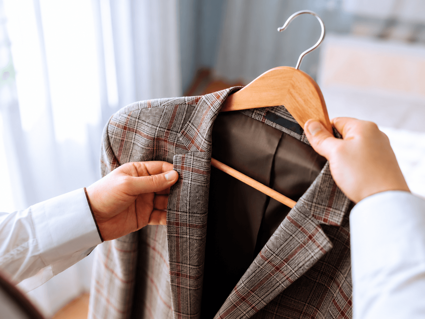 A hand holding up a pressed green shirt on a wooden hanger.